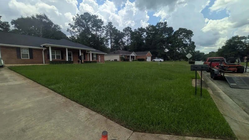 Uncut lawn at a brick home with lawn equipment nearby