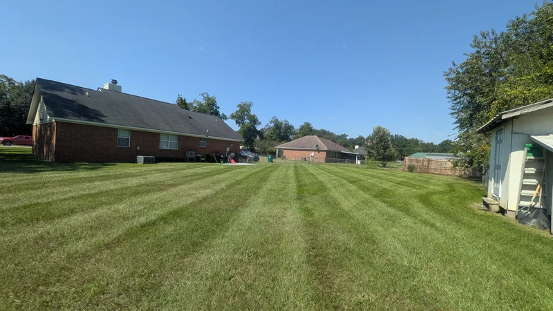 Wide striped lawn beside a single-story brick home